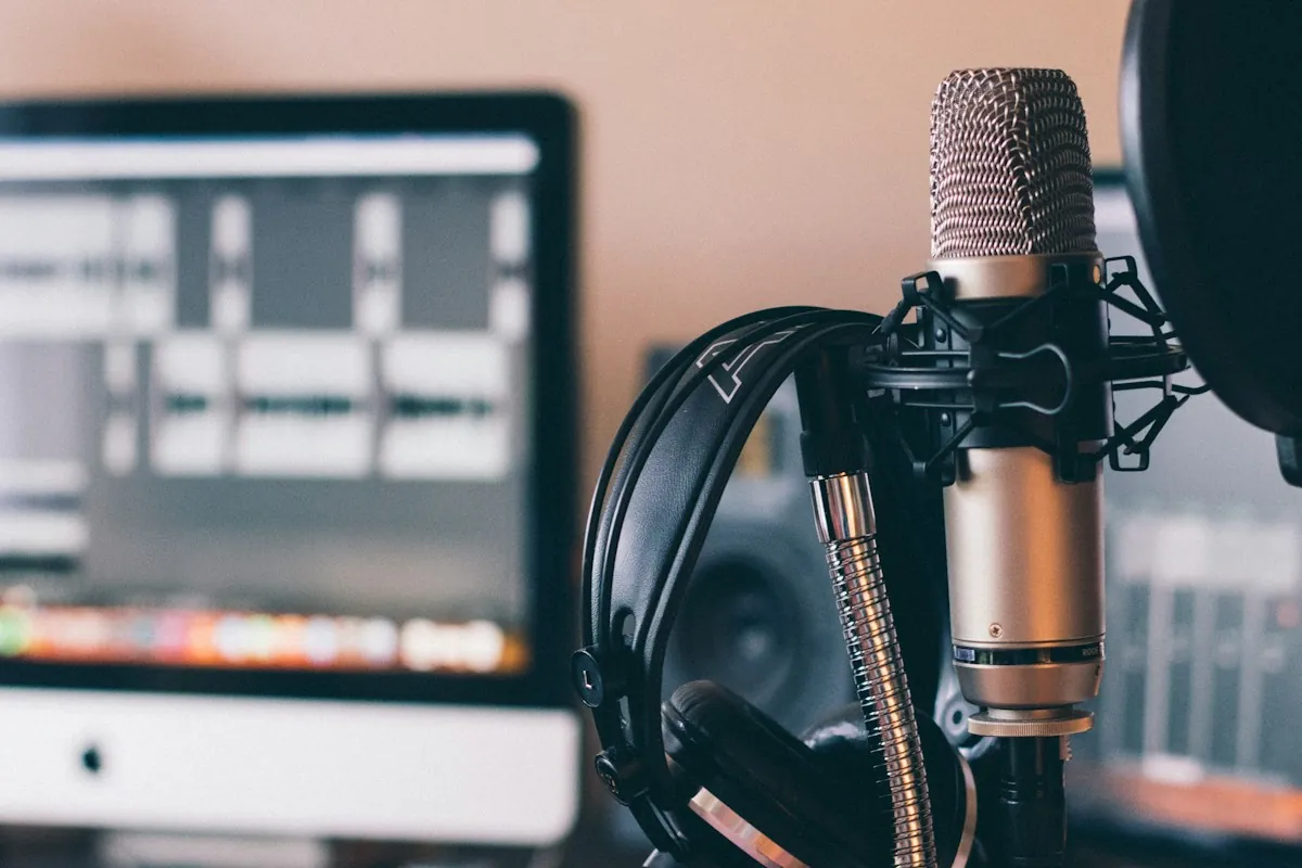 A studio microphone and headphones in front of an audio editing screen, used to record course voiceover in another language