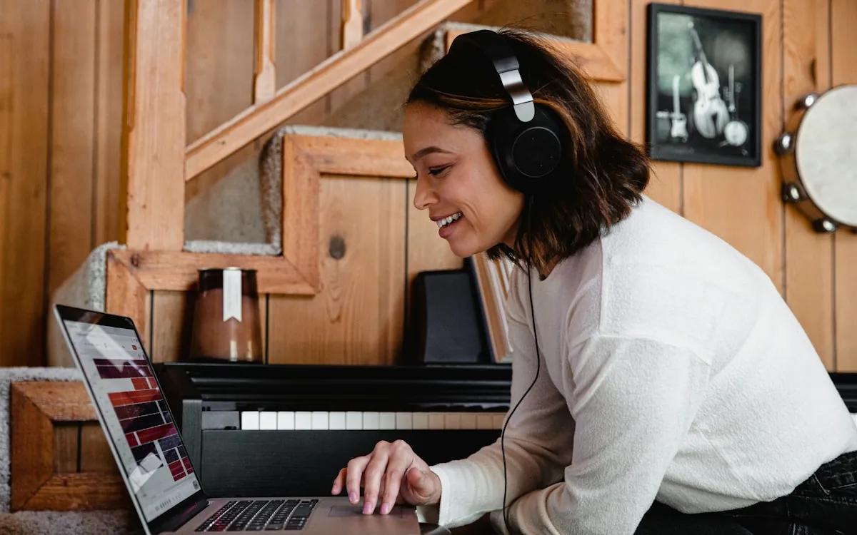 A narrator wearing headphones smiling at a laptop while recording at home